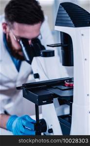 Young Male Researcher Looking At S&les Under Microscope In The Laboratory