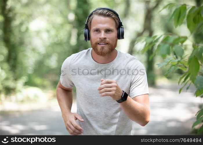 young male runner using headphones runs in nature