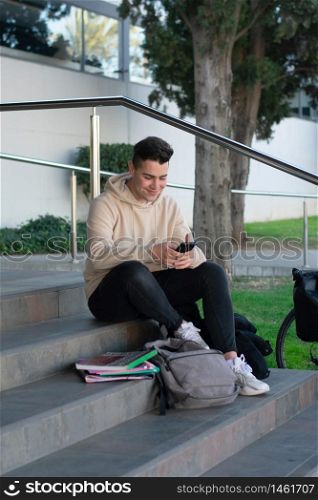 Young male sitting on a campus staircase while using a mobile