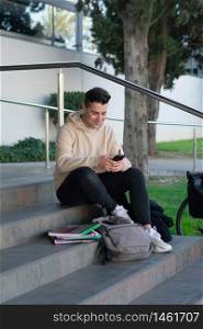 Young male sitting on a campus staircase while using a mobile