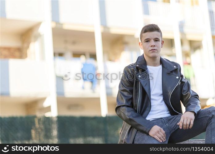 Young male sitting outdoors wearing black leather jacket.
