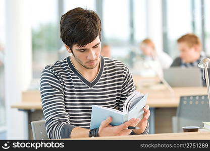 Young male student read book in classroom at high school