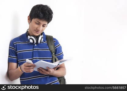 Young male student reading book while leaning on wall