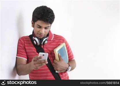 Young male student reading text message on smart phone while leaning on wall