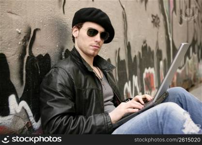 young male student sit laptop outdoor silver graffiti wall
