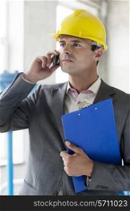 Young male supervisor with clipboard using cell phone in industry