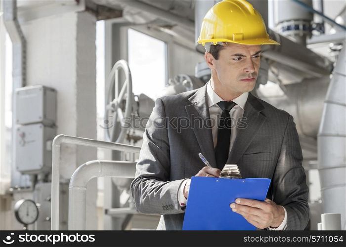 Young male supervisor writing on clipboard in industry