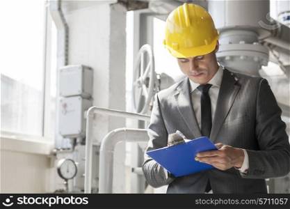 Young male supervisor writing on clipboard in industry