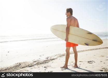 Young male surfer looking out to sea from beach, Cape Town, Western Cape, South Africa