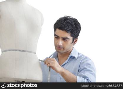 Young male tailor measuring waist of mannequin