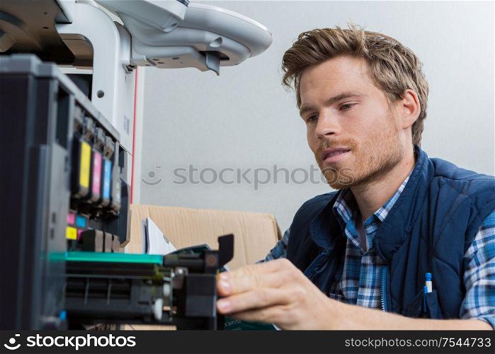 young male technician is repairing a printer at office
