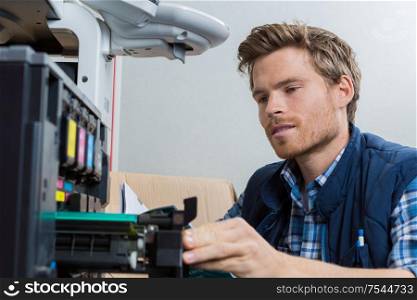 young male technician is repairing a printer at office