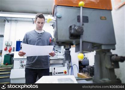 Young male technician looking at blueprint in workshop