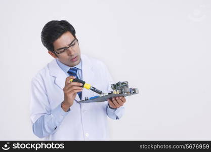 Young male technician repairing circuit board against gray background