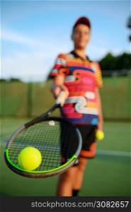 Young male tennis player poses with racket and ball on outdoor court. Active healthy lifestyle, sport game competition, fitness training with racquet. Male tennis player poses with racket and ball