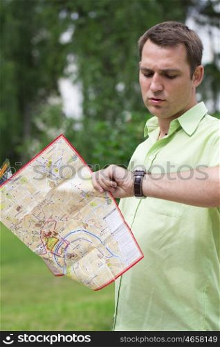 Young male tourist with map in hand looking at wristwatch. Tourist map of the city of Moscow, Russia (no trademark)