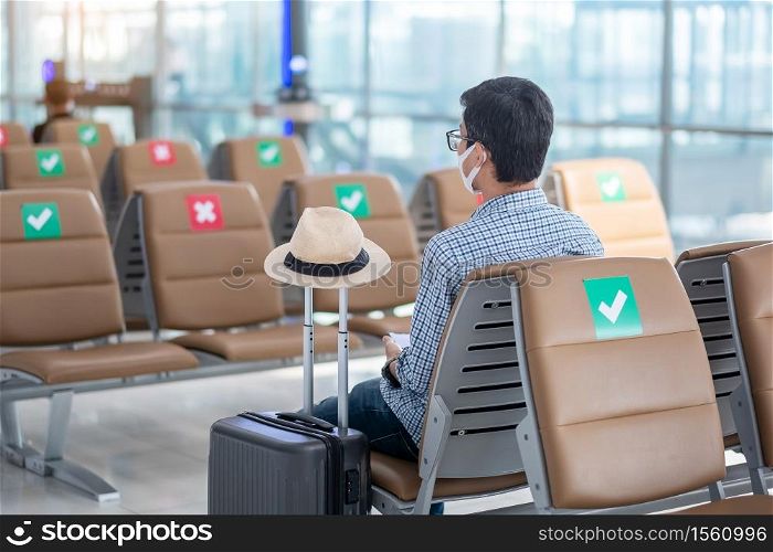 Young male wear face mask sitting on chair in airport terminal, protection Coronavirus disease (Covid-19) infection, Hipster man traveler ready to travel. New Normal and social distancing concepts