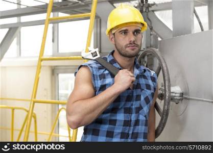 Young male worker with wrench leaning on large industrial valve