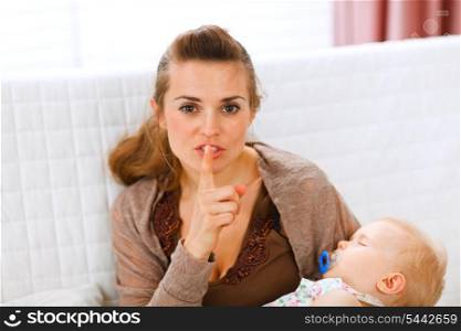 Young mama holding sleeping baby and showing shh gesture at home&#xA;