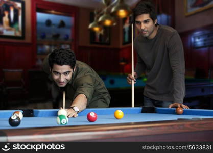 Young man aiming at cue ball while friend standing by pool table