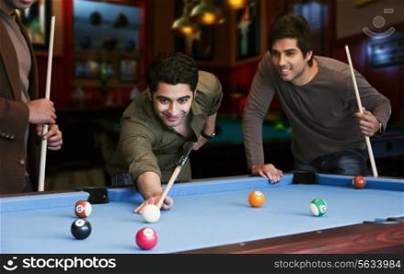 Young man aiming at cue ball while friends standing by pool table