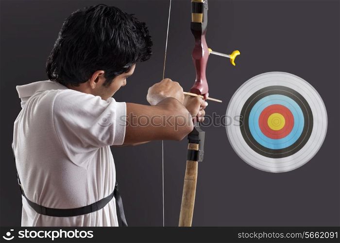 Young man aiming target with bow against black background
