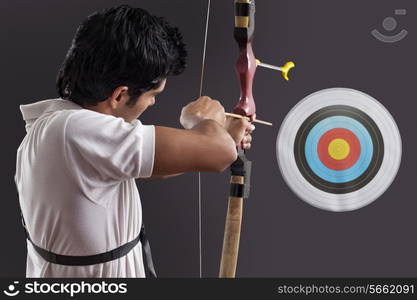 Young man aiming target with bow against black background