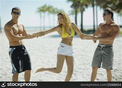 Young man and a mid adult man holding a young woman on the beach