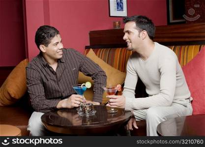 Young man and a mid adult man sitting on a couch holding cocktails