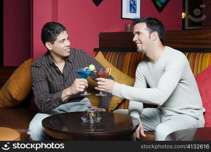 Young man and a mid adult man sitting on a couch toasting with cocktails