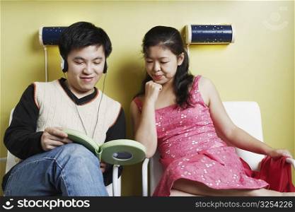Young man and a mid adult woman sitting on chairs listening to music