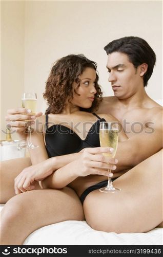 Young man and a teenage girl sitting on the bed holding champagne flutes