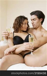 Young man and a teenage girl sitting on the bed holding champagne flutes