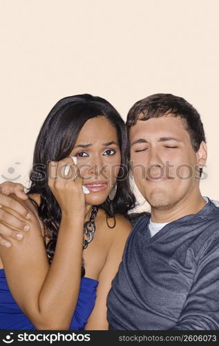 Young man and a teenage girl watching television and crying