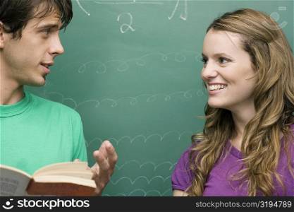 Young man and a young woman talking to each other in a classroom