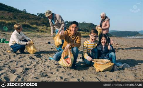 Young man and children posing while picking up trash with group of volunteers on the beach. Young man and children cleaning the beach