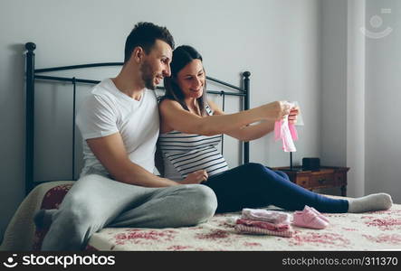 Young man and his pregnant wife looking baby girl clothes. Man and pregnant woman looking baby clothes