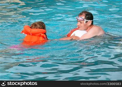 young man and little girl in lifejacket bathing in pool on resort