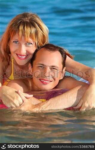 young man and nice women lying on an inflatable mattress in pool, woman lying astride man
