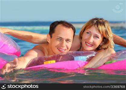 young man and nice women lying on an inflatable mattress in pool, man extended hand forward