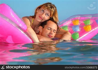 young man and nice women lying on an inflatable mattress in pool, man closed eyes