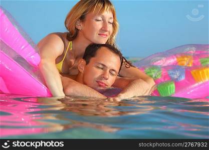 young man and nice women sleep on an inflatable mattress in pool, closed eyes