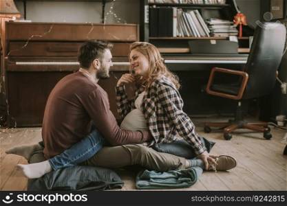 Young man and pregnant woman sitting on the floor in the room