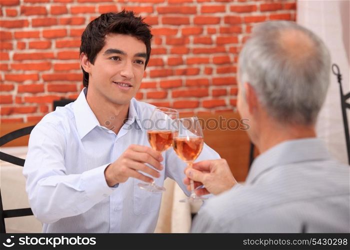 Young man and senior chinking wine glasses