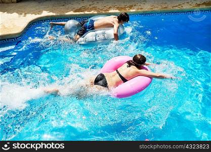 Young man and teenage sister racing on inflatables in swimming pool