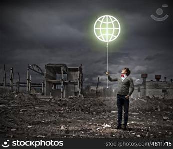 Young man and the symbol of our planet. Young man and the symbol of our planet against polluted and ruined landscape