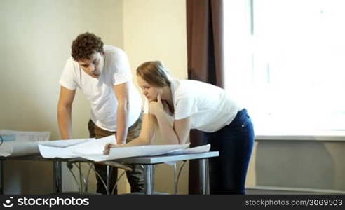 Young man and woman architects working with plans discussing the details of their project