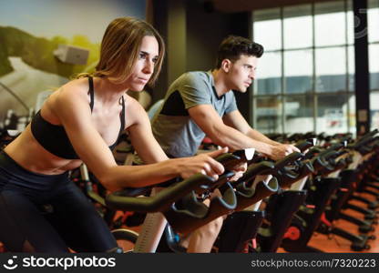 Young man and woman biking in the gym, exercising legs doing cardio workout cycling bikes. Two people in a cyclo indoor class wearing sportswear.. Couple in a cyclo indoor class wearing sportswear.