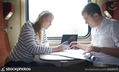 Young man and woman busy with discussion of drawing during business journey in the train