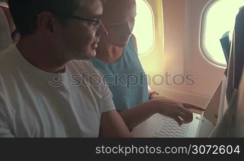 Young man and woman busy with work during the flight. Man talking and showing what to do, woman making corrections while working with laptop